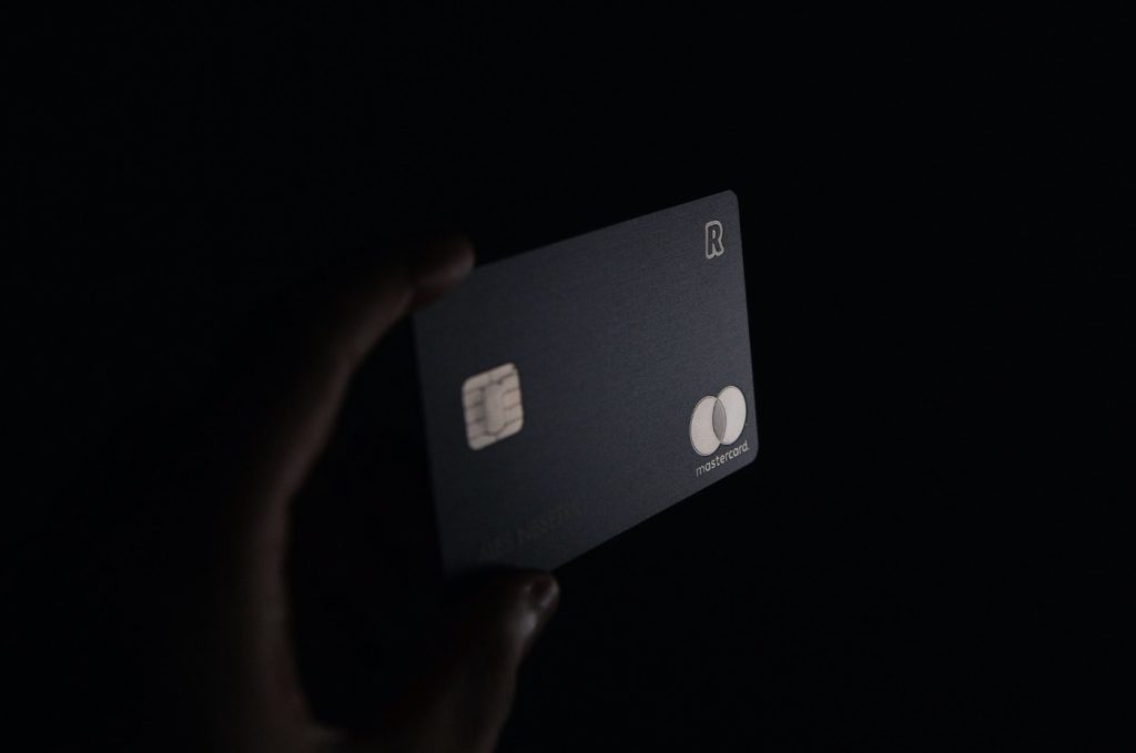 Close-up of a hand holding a matte black credit card in front of a dark background.