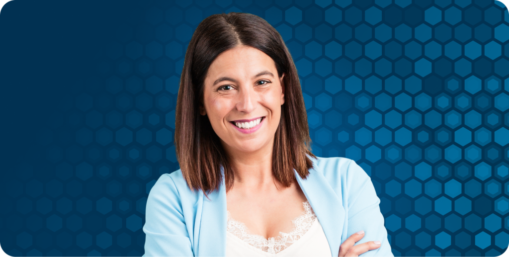 Woman in front of blue hexagonal background stands smiling at the camera.