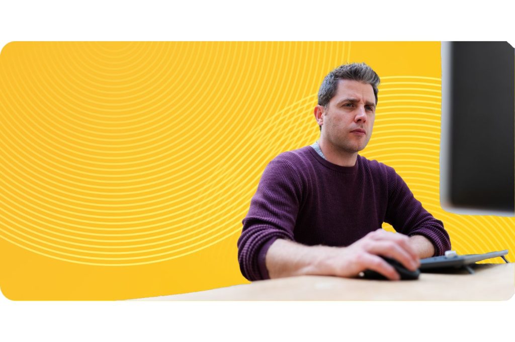 A CTO sits at a desktop with his hand resting on the mouse in the foreground of a bright yellow spiral background.