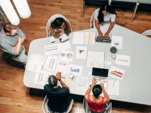 Five people sit around a table seen from above. The table is covered with business papers.