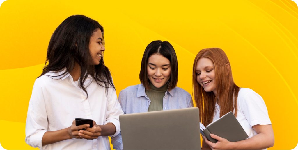 Three engineers stand together and look toward the engineer in the center holding a laptop.