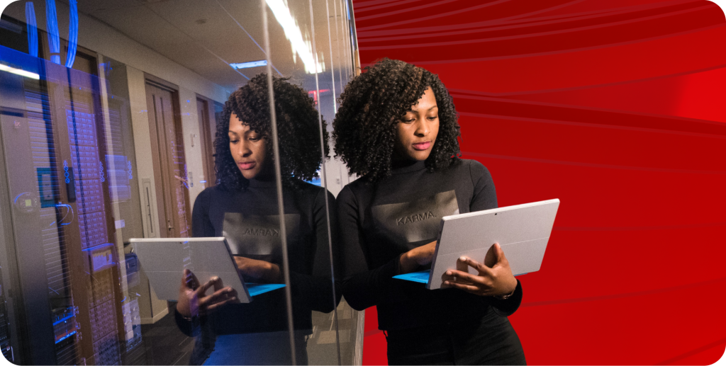 Woman leans against a glass wall holding a laptop.