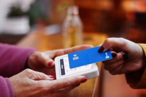 A woman holds her credit card over a point-of-sale device being held by another woman.