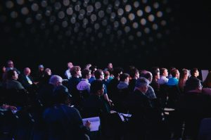 A crowd of people watches a presentation at a conference
