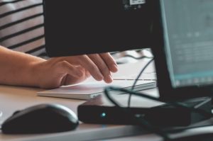 Close up of a hand hovering over a trackpad, with the back side of a computer monitor visible in the foreground.