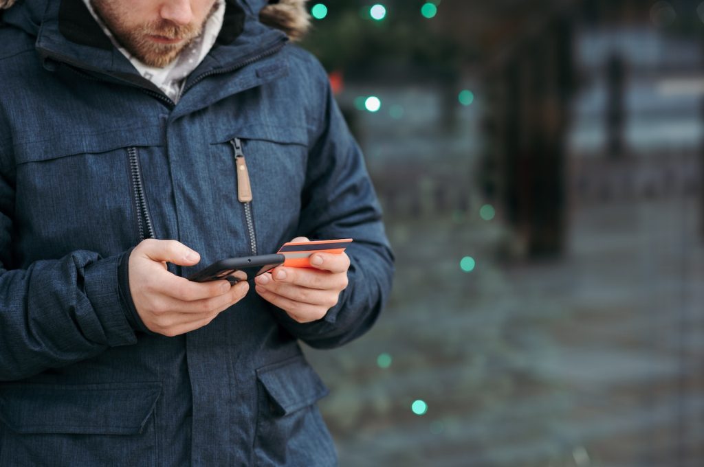 A customer types in his credit card number into an app on his mobile phone in order to make a purchase.