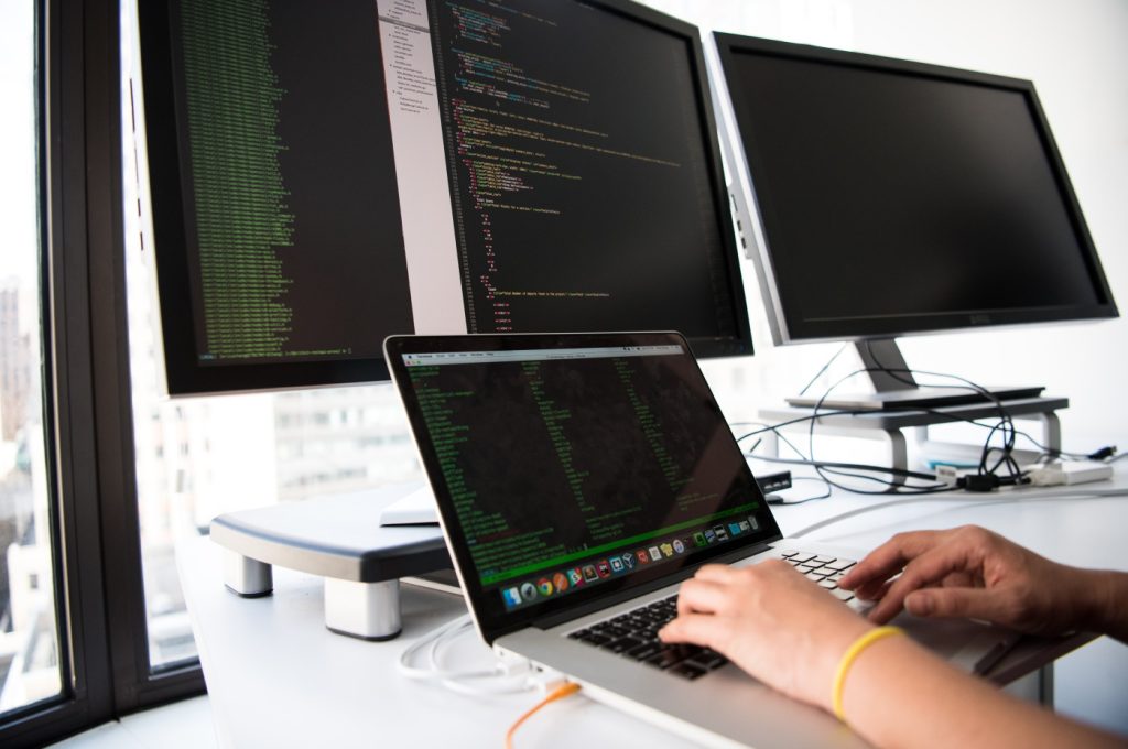 Engineer sitting in front of three computer screens filled with code.