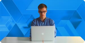 CTO sits in front of a blue geometric background at a laptop.
